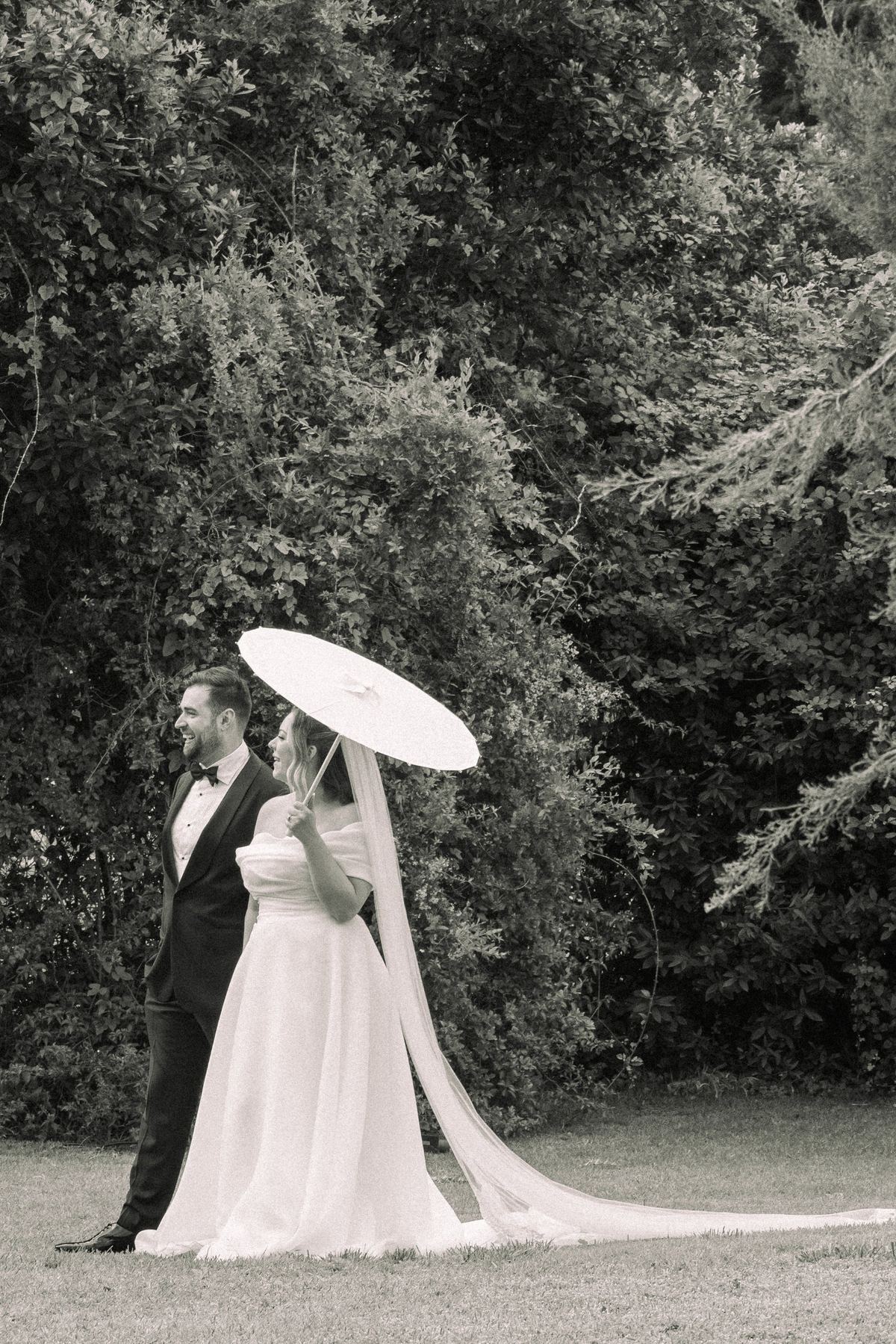 Novios paseando por el jardín con una sombrilla en su boda en la Finca Molino del Duque, Estepona