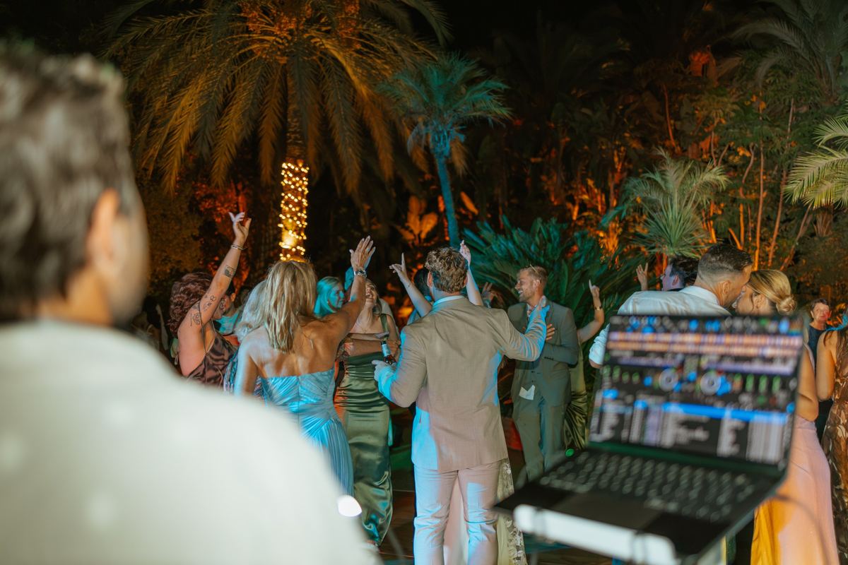 Invitados bailando frente a la cabina del DJ de Live Marbella en una fiesta nocturna entre palmeras